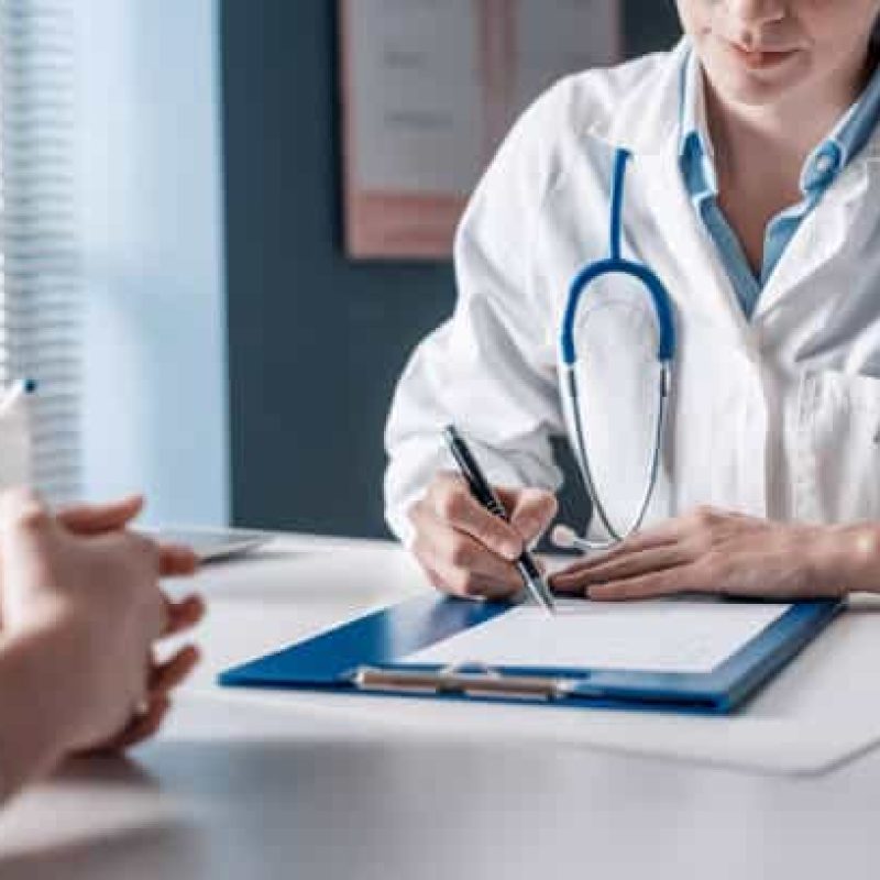 Doctor sitting at desk and writing a prescription for her patient